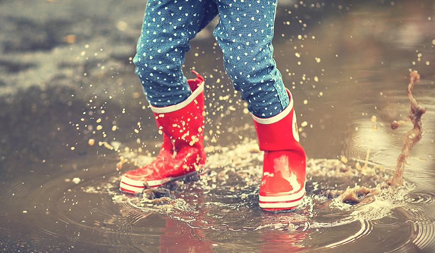 Child’s rubber boots-clad legs jumping in a puddle