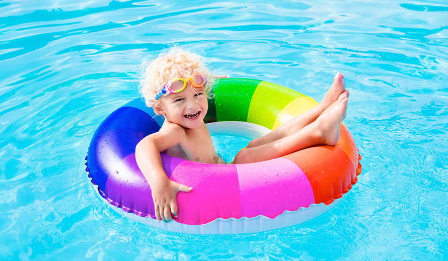 Happy little boy on a rainbow-striped floatie in a swimming pool.