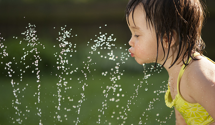 Little girl cools off by drinking from sprinkler.