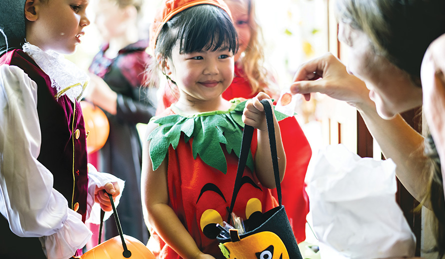 A little girl dressed as a pumpkin gets candy on Halloween.