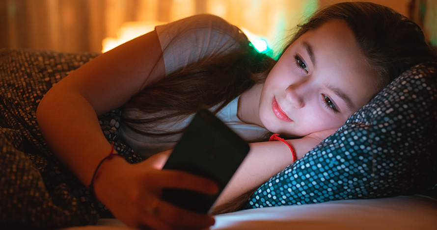 Una joven hispana mira fijamente su teléfono mientras está en la cama.