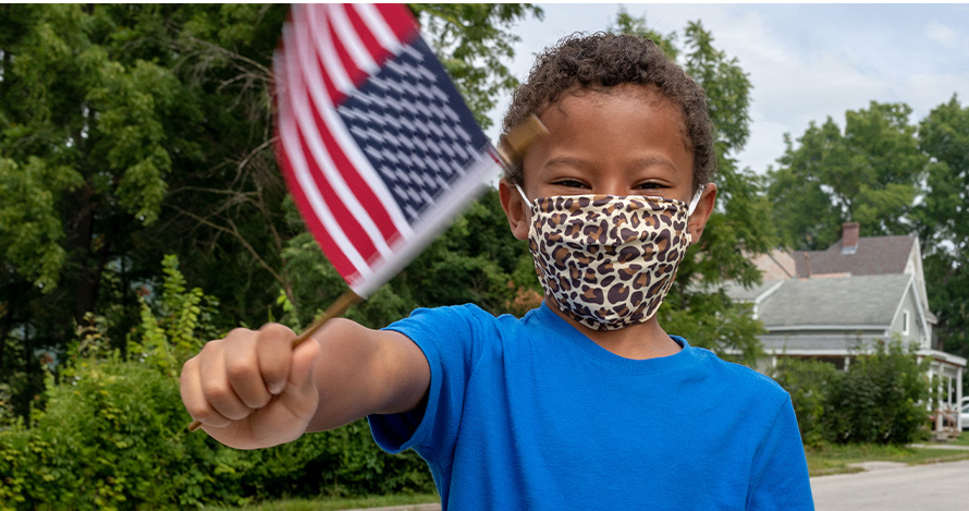 A young boy waves an American flag with a mask on.