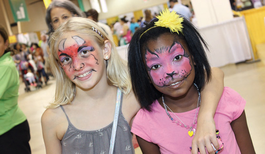 Two smiling young girls with painted faces, one a demon and one a cat, at the Family Expo.