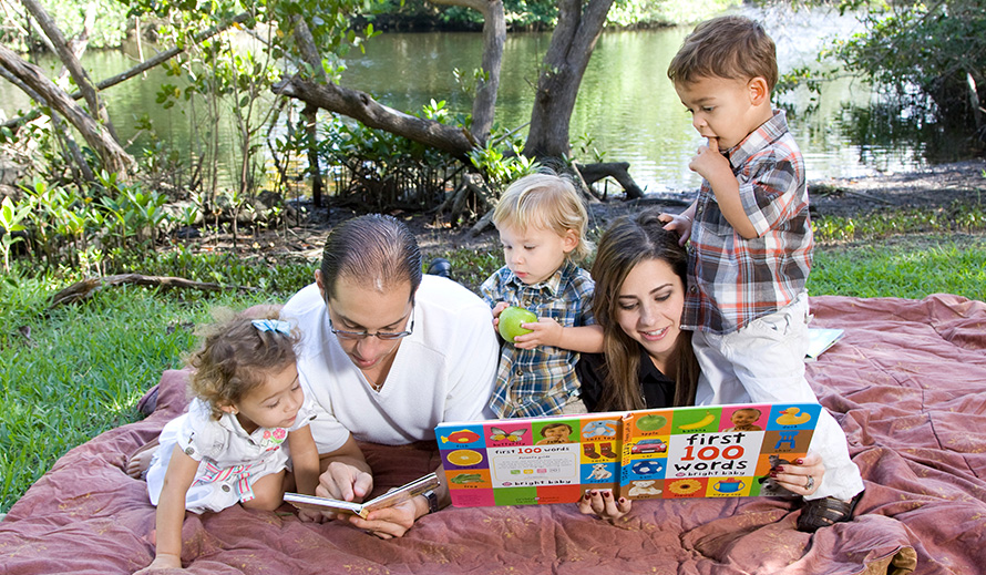 Family reading on a blanket at the park.