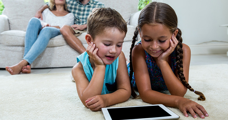 Dos niñas pasan tiempo frente a la pantalla en casa mientras los padres observan.