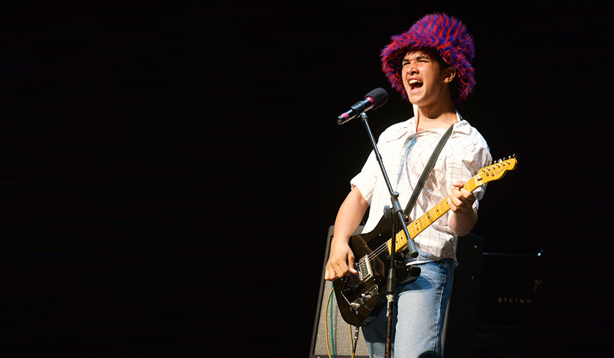 Teen boy onstage singing and playing electric guitar