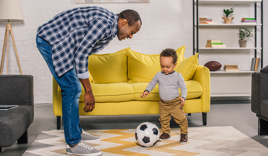 A father and son practice soccer inside the home.