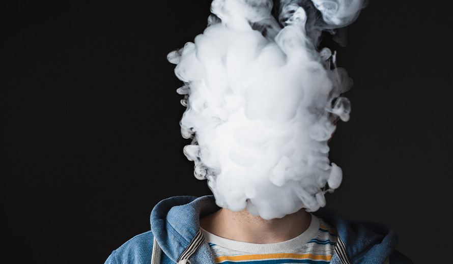 A teen’s face is completely obscured by smoke from an e-cigarette.