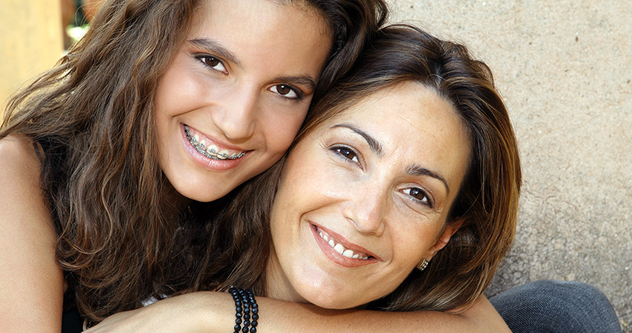 Teen daughter with arm around mother, both smiling 