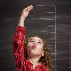Young child reaching up to measure height on ruler drawn with chalk on wall.