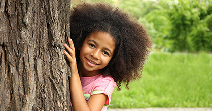 Shy little girl peering out from behind a tree.