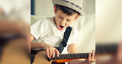 Little boy singing and playing a guitar.