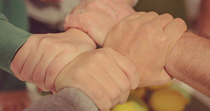 Four hands interlocking together on wrists.