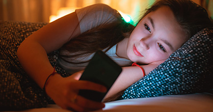 A young Hispanic girl stares at her phone while in bed. 