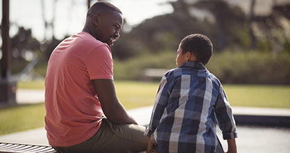 An African American father speaks with his son on a bench. 