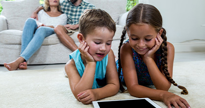 Two young girls spend some screen time at home while parents look on. 