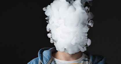 A teen’s face is completely obscured by smoke from an e-cigarette.